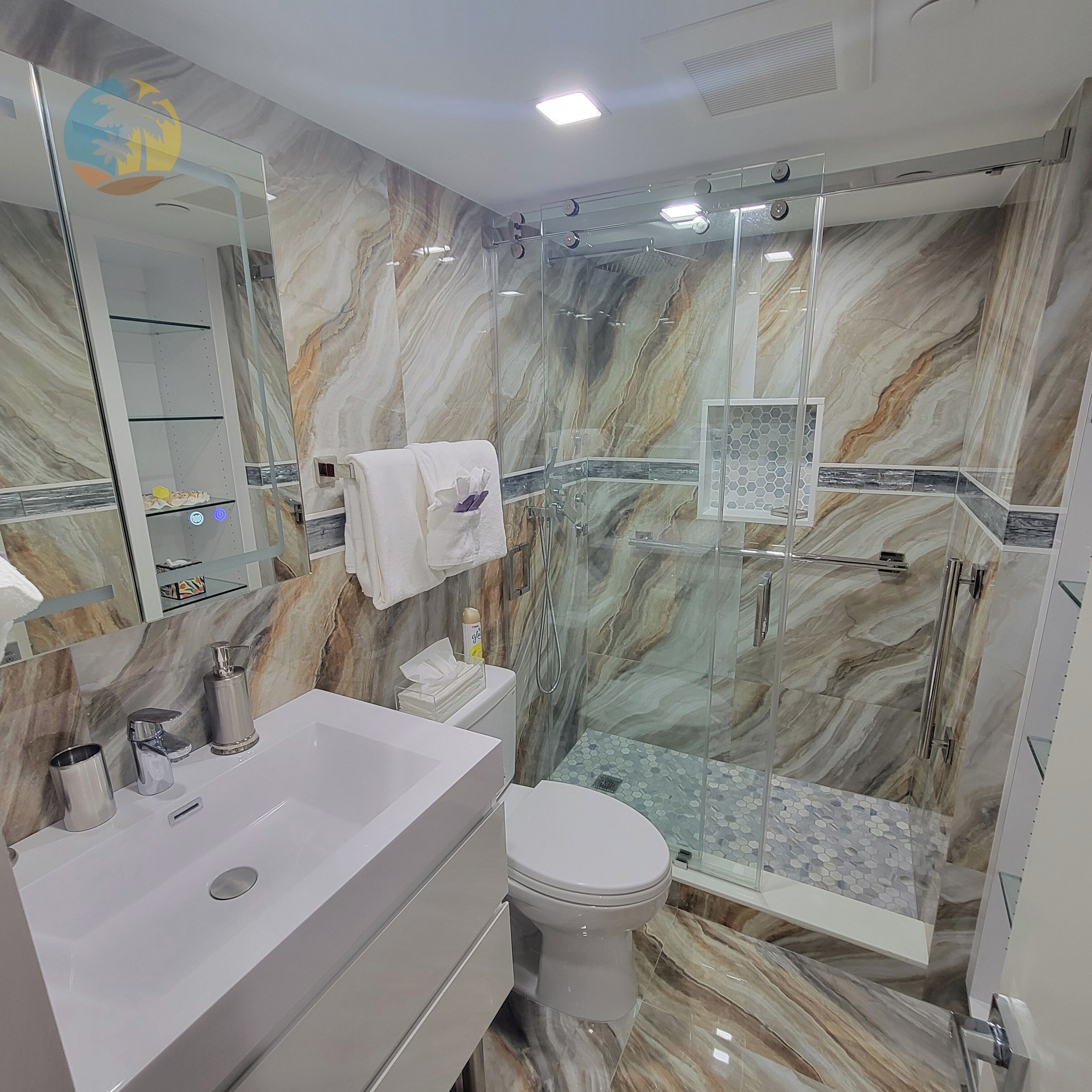 Een moderne badkamer met een marmeren spatwand, een glazen douchecabine, een wit wastafelmeubel en een toilet.