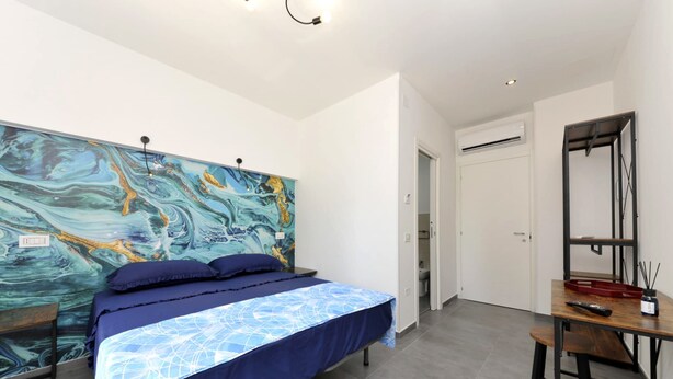 A bedroom with a bed, a desk, and a large abstract painting on the wall. - MaryGiò - Blue Room (Salerno)