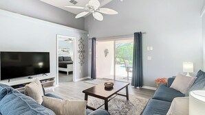 Ein modernes Wohnzimmer mit Flachbildfernseher, Deckenventilator, Sofagarnitur und Essbereich mit Tisch und Stühlen.