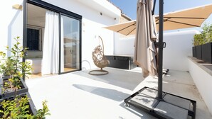 Eine moderne Außenpatio mit Glastür zu einem Raum, einem dekorativen Stuhl und einem großen Sonnenschirm.