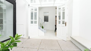 Ein helles, weißes Interieur mit einer Treppe, die zu einer zweiten Etage führt, einer Tür mit Schlüsselloch und einer Pflanze auf dem Boden.