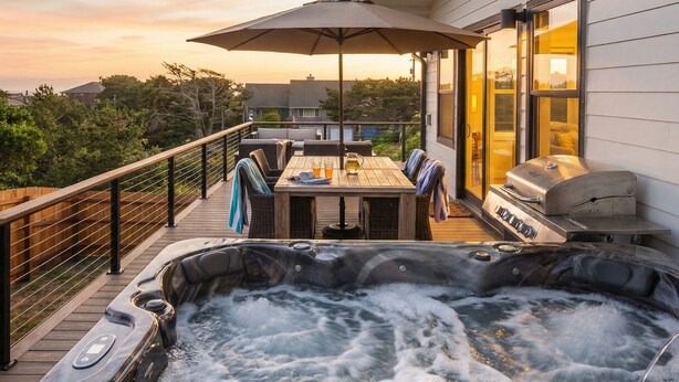 Ein Whirlpool auf einer Holzterrasse mit Tisch, Stühlen, Sonnenschirm und Grill.