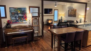 A cozy living room with a piano, a fireplace, a dining area, and a kitchen. - Perfect location! Downtown Beach & Ski Pad w/hot tub in the heart of Sandpoint. (Sandpoint)