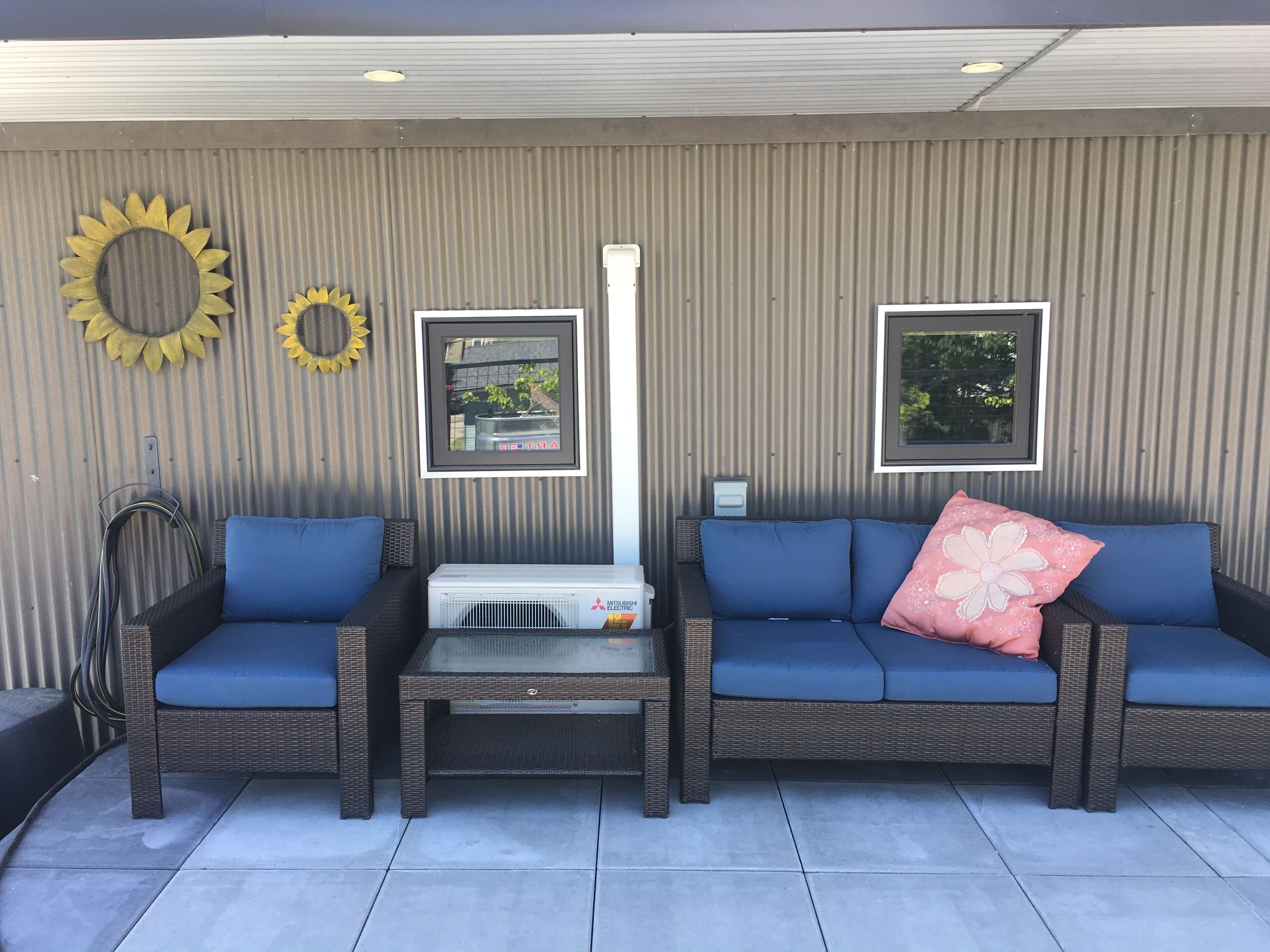 A covered patio area with two blue cushioned sofas, a table, and a wall-mounted heater.