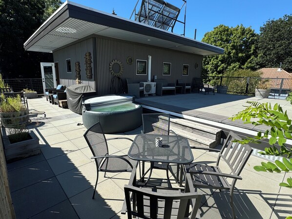 Un patio exterior con un jacuzzi, zona de estar y un edificio con techo inclinado.