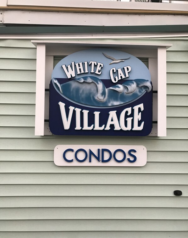 A sign for 'White Cap Village Condos' with a wave design.