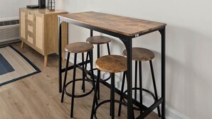 Een moderne keuken met een houten tafel, barstoelen, twee hangende rieten lampen, een flatscreen televisie en een raam met uitzicht.