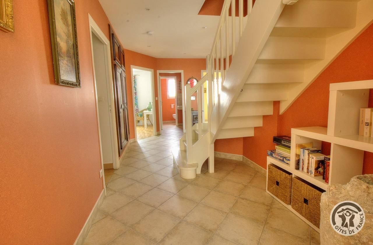 Un couloir avec un escalier blanc, une bibliothèque et une porte donnant sur une autre pièce.