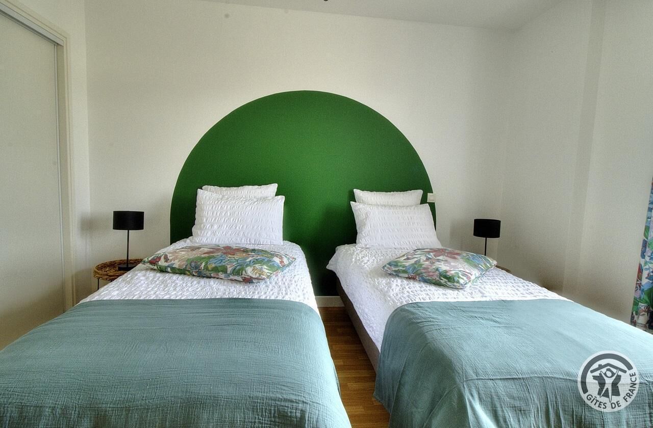 Ein Zimmer mit zwei Einzelbetten, beide mit grünem Kopfteil und weißer Bettwäsche. Es gibt zwei Nachttische mit Lampen, und einen großen, grünen Bogen über den Betten.
