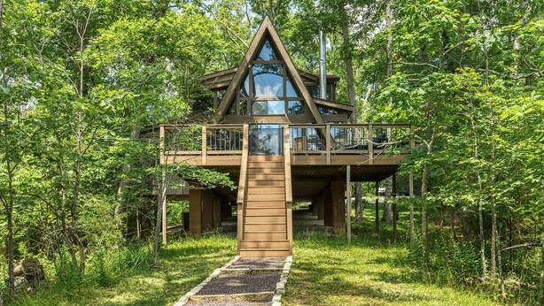 A wooden cabin with a glass balcony, surrounded by dense forest. - Lakefront Chalet w/ Fire Pit (Innsbrook)