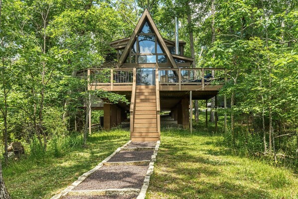 A wooden cabin with a glass balcony, surrounded by dense forest. - Lakefront Chalet w/ Fire Pit (Innsbrook)