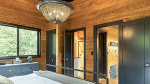 A bedroom with a bed, bedside table, and a large window. There is a chandelier hanging from the ceiling and a door leading to another room. - Lakefront Chalet w/ Fire Pit (Innsbrook)