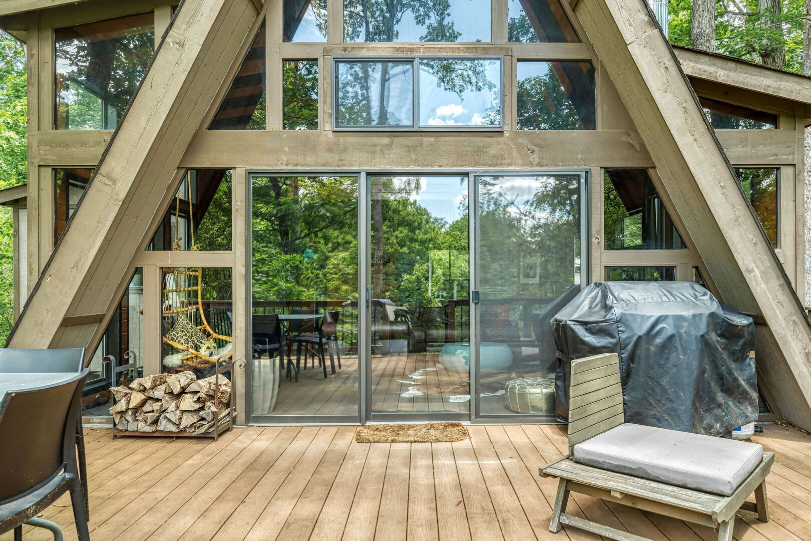 A wooden deck with a glass door leading to a patio area, outdoor furniture, and a covered grill.