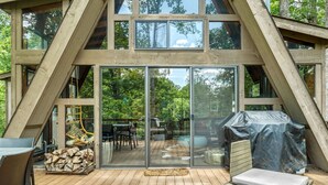 A wooden deck with a glass door leading to a patio area, outdoor furniture, and a covered grill. - Lakefront Chalet w/ Fire Pit (Innsbrook)