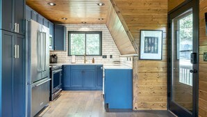 A modern kitchen with dark blue cabinets, stainless steel appliances, and a wooden ceiling. - Lakefront Chalet w/ Fire Pit (Innsbrook)