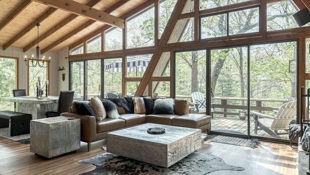 Un vaste espace de vie doté d’un grand plafond en bois, d’un canapé en cuir, d’une table basse et offrant une vue sur l’extérieur grâce à de grandes fenêtres.