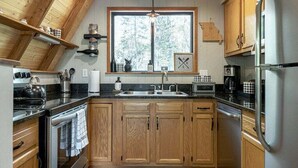 Une cuisine avec des meubles en bois, un réfrigérateur en acier inoxydable et une fenêtre donnant sur les arbres.