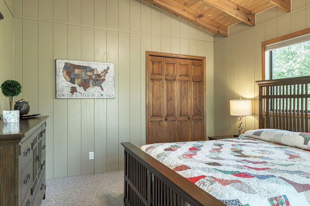 A bedroom with a wooden bed, a quilt, a wooden wardrobe, a map on the wall, and a window with a view of trees.