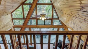 Una cabaña de madera con techo triangular, ventanas amplias y un ventilador de techo.