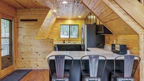 Una cabaña con interior de madera, una cocina y un comedor con tres sillas de metal.