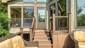 Una terraza de madera con mobiliario exterior, una escalera y ventanas amplias.