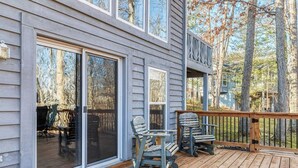A wooden deck with two Adirondack chairs, a sliding glass door, and a view of trees. - Innsbrook Home | Lake + Resort Access (Innsbrook)