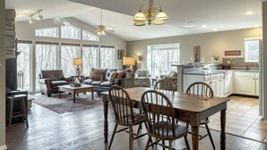 A spacious living room with a dining area, large windows, and a kitchen in the background. - Innsbrook Home | Lake + Resort Access (Innsbrook)