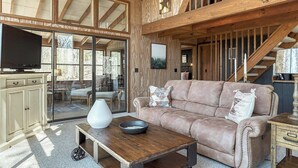 Un salón espacioso con techo de madera, un ventanal grande, un sofá, una mesa de centro y un televisor.