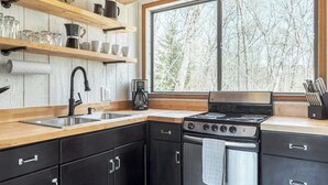 Una cocina moderna con armarios negros, un lavamanos de acero inoxidable y un amplio ventanal con vistas a árboles.