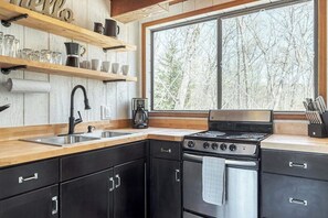 A modern kitchen with black cabinets, a stainless steel sink, and a large window offering a view of trees.