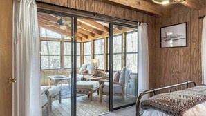 Una habitación tipo cabaña de madera con una puerta corrediza de vidrio que da a un espacio exterior con mobiliario.