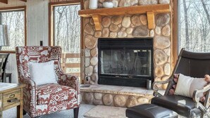 Una habitación acogedora con chimenea de piedra, vigas de madera y ventanas amplias.