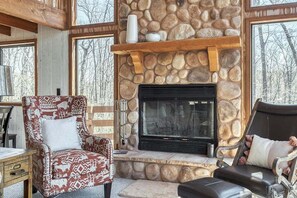 A cozy room with a stone fireplace, wooden beams, and large windows.