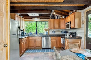 A kitchen with wooden cabinets, a stainless steel refrigerator, a dishwasher, and a window providing a view of greenery.