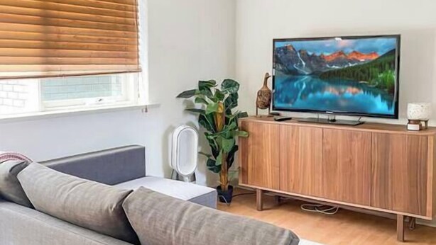 A modern living room with a grey sofa, wooden cabinet, and a flat-screen TV on a stand. - Carlton North Private Abode (Carlton North)
