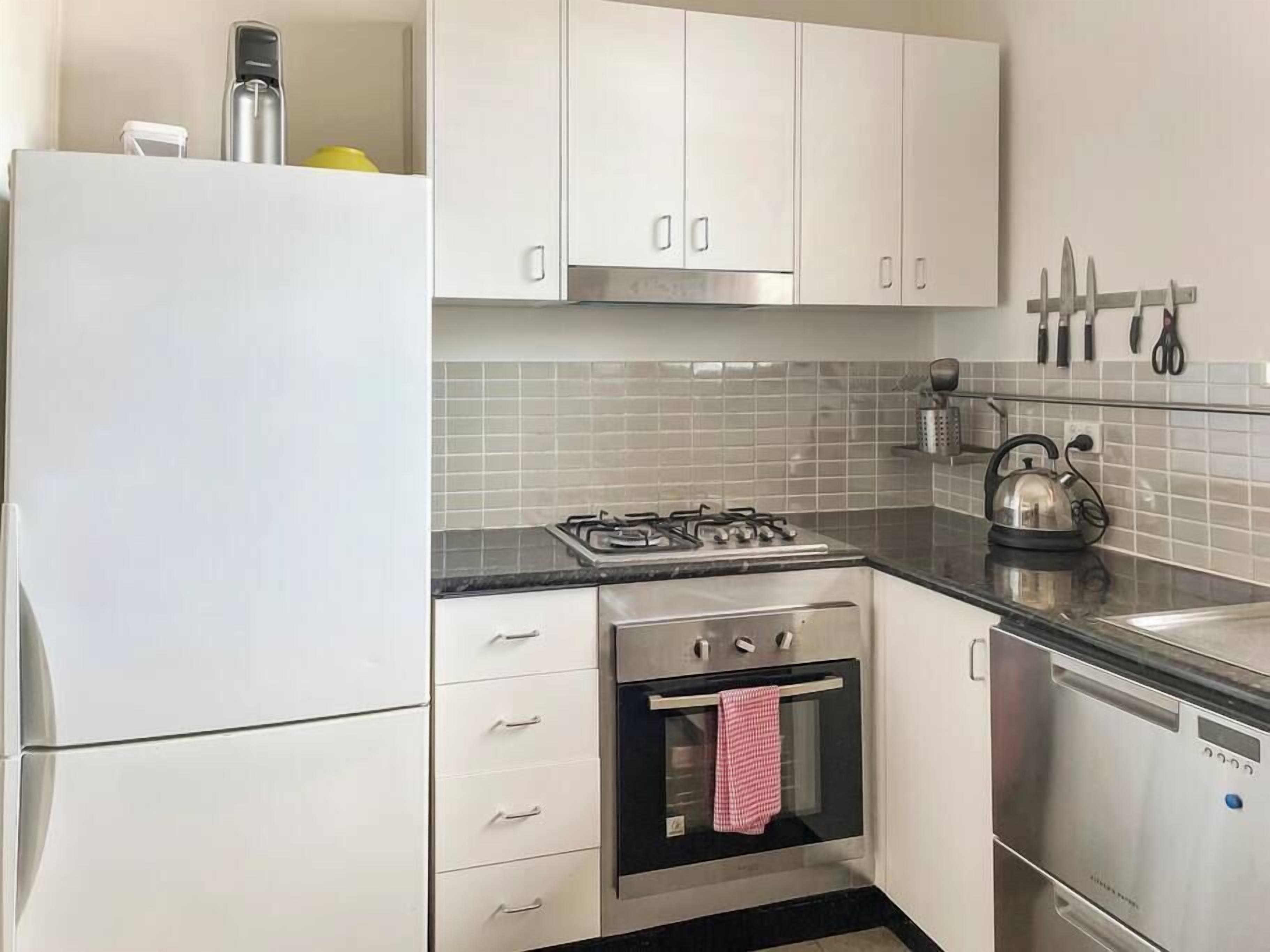 Une cuisine de taille réduite avec des meubles blancs, une cuisinière à gaz, un four et un lave-vaisselle.