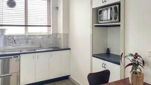 A modern kitchen with white cabinets, a stainless steel sink, and a microwave on a shelf. - Carlton North Private Abode (Carlton North)