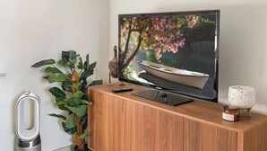 A modern living room with a wooden cabinet, a flat-screen TV, a potted plant, and a small table with a candle. - Carlton North Private Abode (Carlton North)