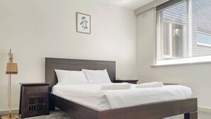 A modern bedroom with a large bed, a bedside table, a lamp, and a window. - Carlton North Private Abode (Carlton North)