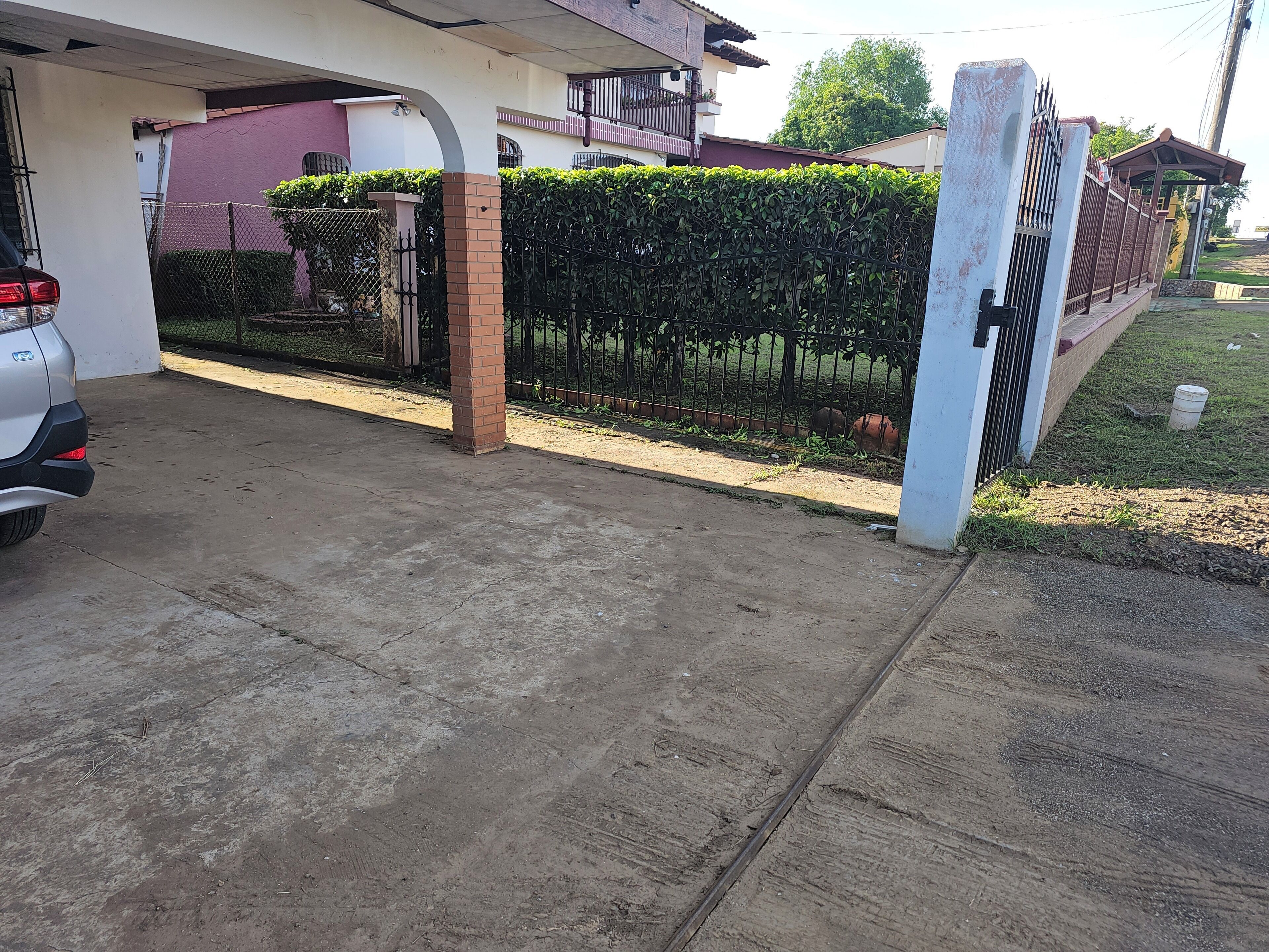 Una entrada con portón y un camino de hormigón que lleva a un edificio con pared rosa y un balcón.