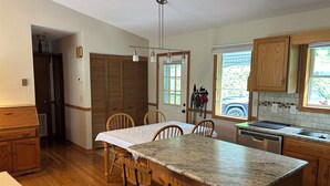 A kitchen with a wooden island, wooden chairs, a dining table, a built-in oven, and a window with a view of the outside. - Beautiful Misty Mountain Views from a quaint cottage in Maggie Valley! (Maggie Valley)