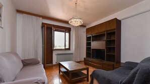 Ein Wohnzimmer mit einer Couch, einem Tisch, einer TV-Konsole und einem Kronleuchter.