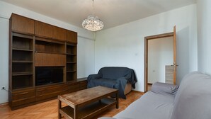 Ein Wohnzimmer mit einer Holzunterhaltungsecke, einem grauen Sofa, einem blauen Sessel und einem Couchtisch aus Holz.