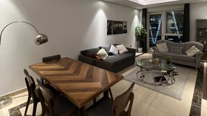 A modern living room with a wooden dining table, two sofas, and a glass coffee table. - 3-bedroom hostel in lovely Dubai with Wi-Fi, AC, fitness room, breakfast (Dubai)