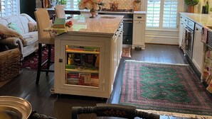 A cozy kitchen with a central island, a dining area with a sofa and chairs, and a view of the outdoors through large windows. - Designer Decorated Estate in Historic Downtown Lewisburg, West Virginia (Lewisburg)