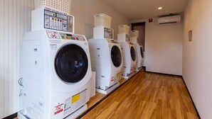 A row of white front-loading washing machines in a hallway with wooden flooring and white walls.