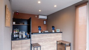 A reception area with a coffee machine, a bulletin board, and a counter with a sign.