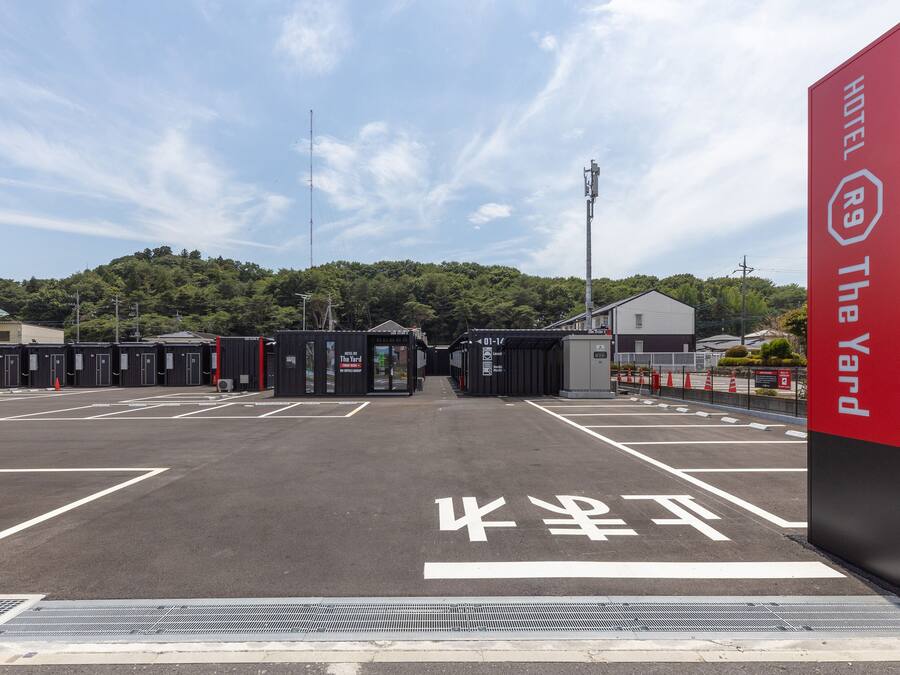 Hoteleingang mit rotem Schild, mehreren Zimmern und einem Parkplatz.