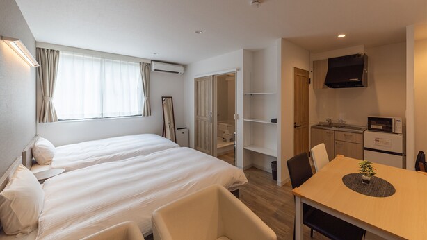 A hotel room with two beds, a dining table, a TV, and a kitchenette.