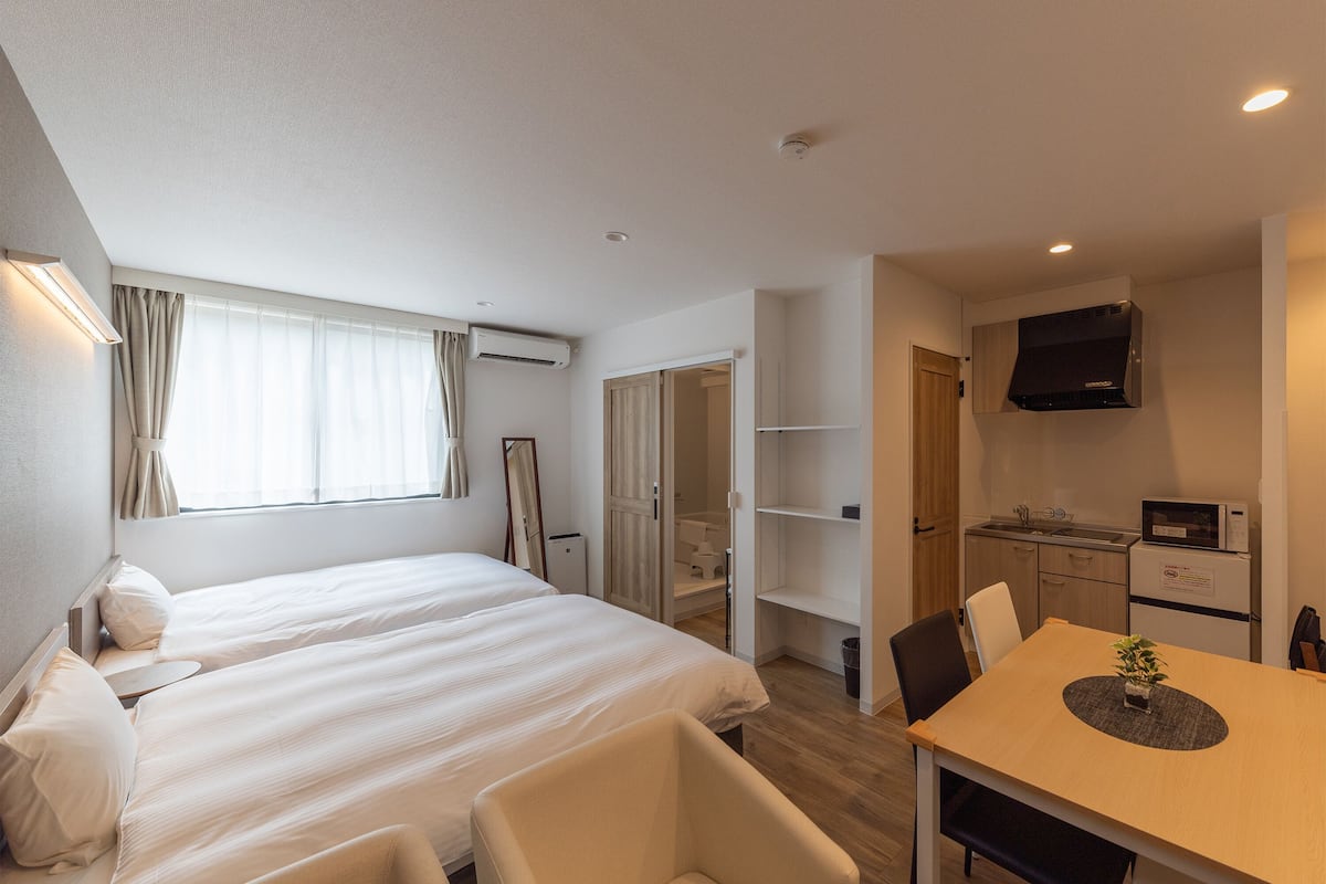 A hotel room with two beds, a dining table, a TV, and a kitchenette.